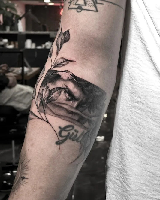 man eyes portrait black and grey realism tattoo with leaves