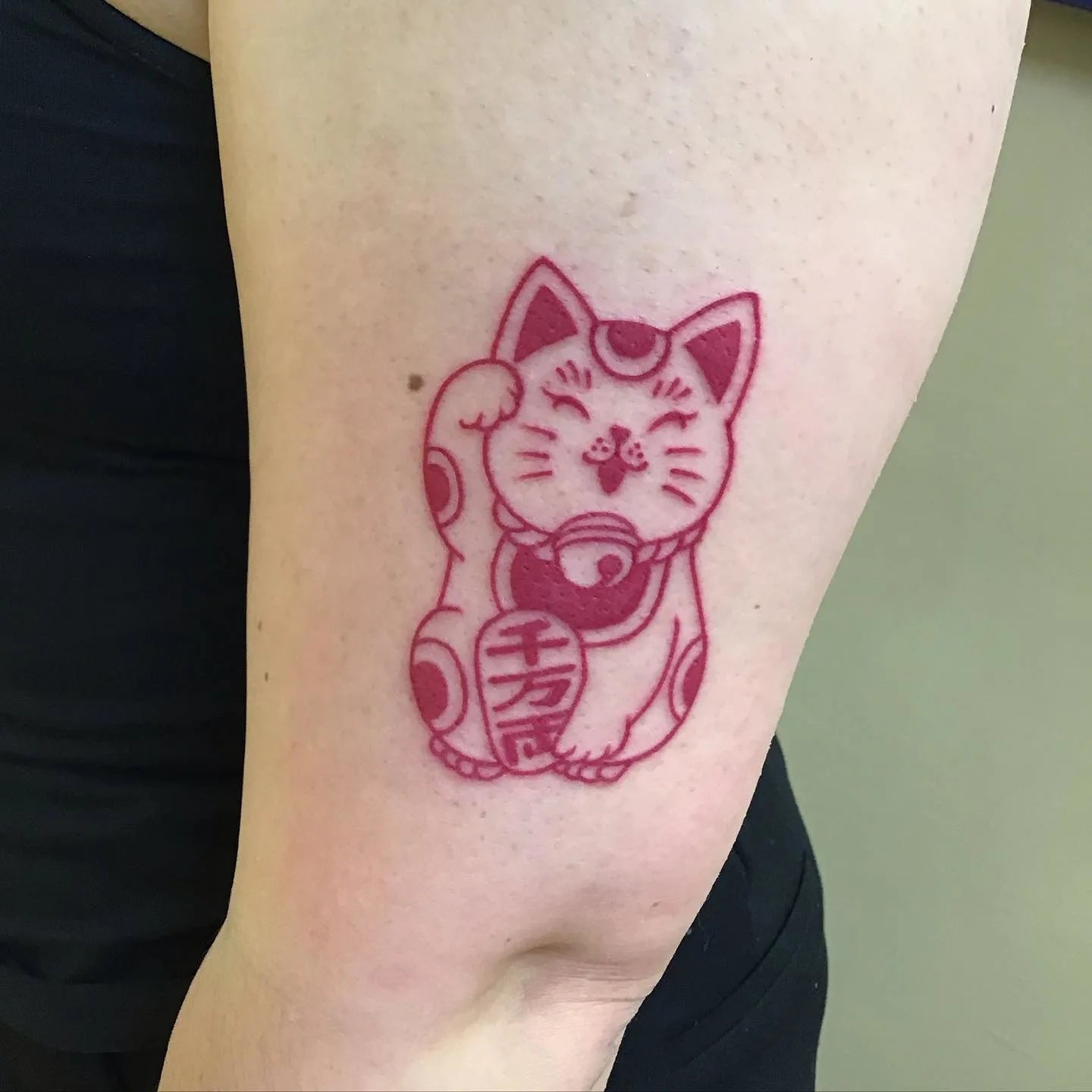 red Japanese lucky fortune waving cat on woman upper arm