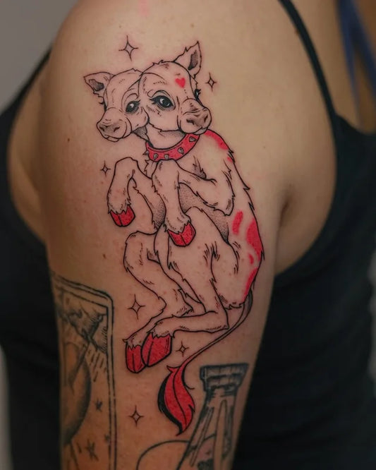 two headed goat with red accents illustrative tattoo on woman upper arm