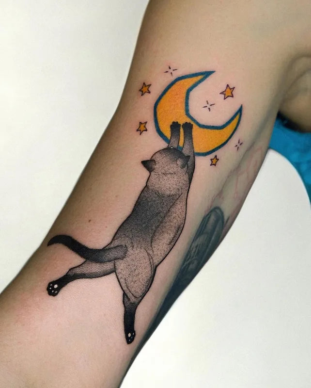 grey cat catching the moon colorful tattoo on woman bicep