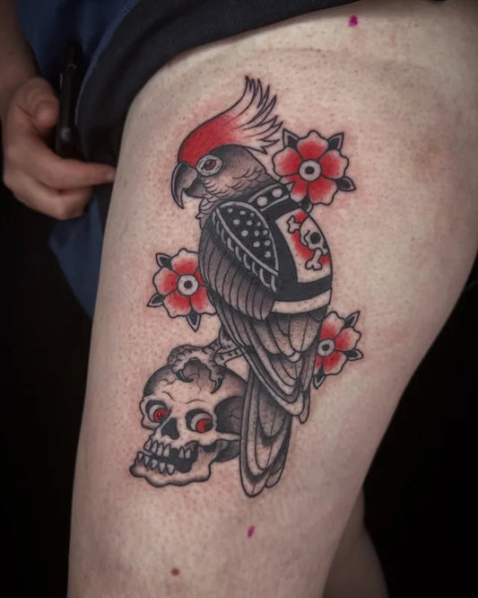 Tattoo of a parrot with flowers and a skull on thigh