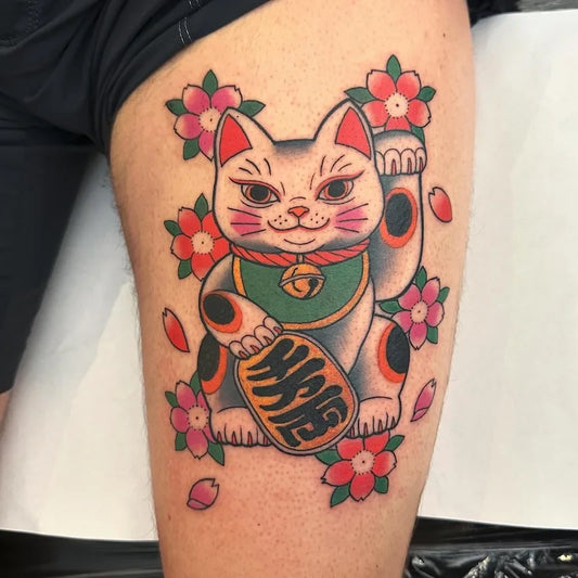 Colorful traditional tattoo of a maneki-neko lucky cat on man thigh
