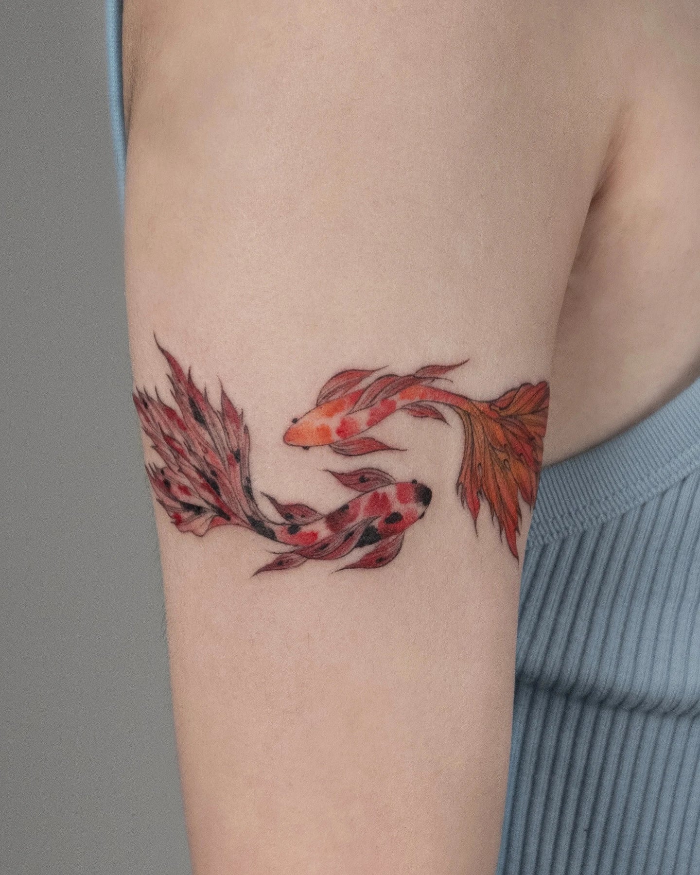a pair of orange gold fish koi fish tattoo on woman upper arm