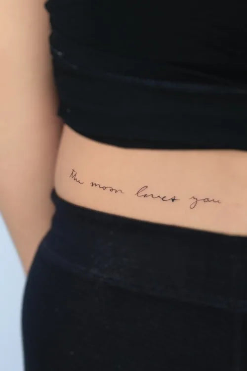 the moon loves you lettering tattoo on waist