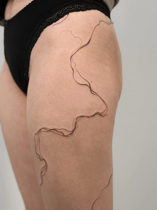 abstract fine line woman thigh tattoo