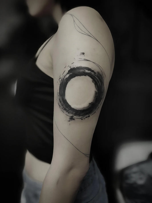 blackwork zen circle brush stroke tattoo on woman upper arm