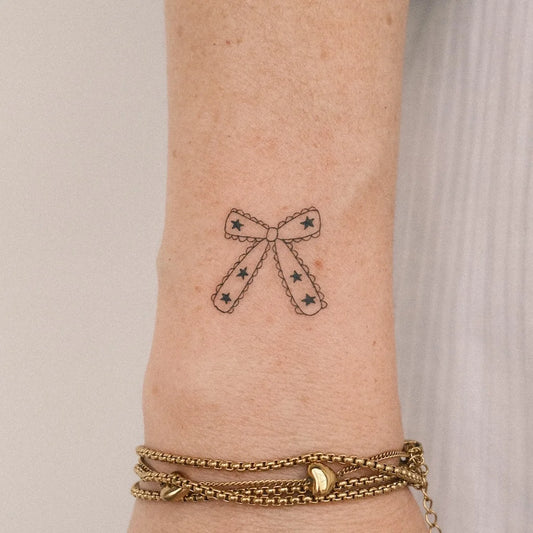 minimalist fine line bowtie outline tattoo on wrist