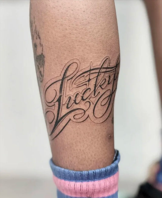 Lucky calligraphy font lettering black tattoo on calf leg