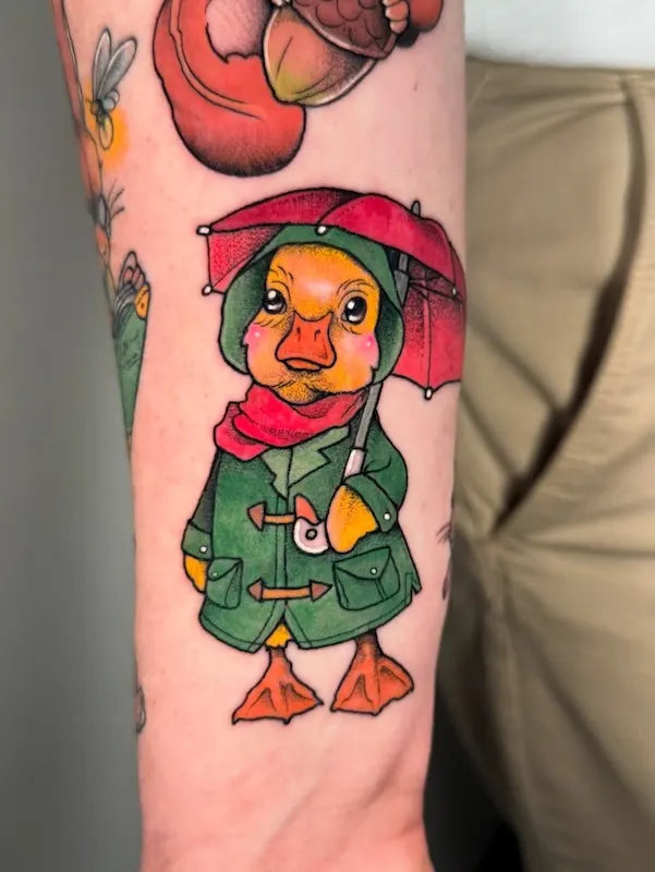 Colorful tattoo of a duck character with a raincoat and umbrella on forearm