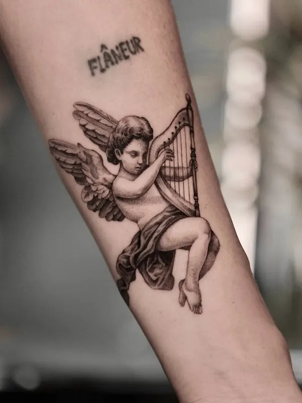black and grey realism tattoo of an cherub angel playing a harp on forearm