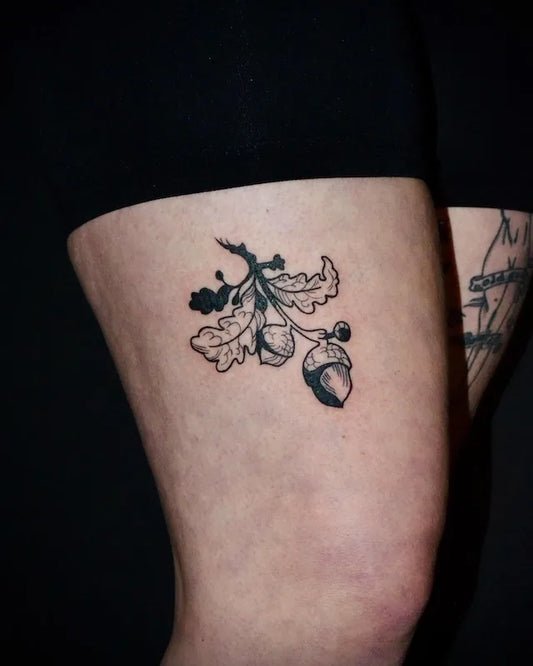 black and white tattoo of an oak leaf and acorn on thigh