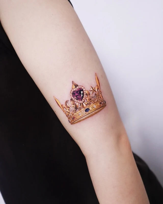 realistic golden crown with gemstone color realism tattoo on woman arm