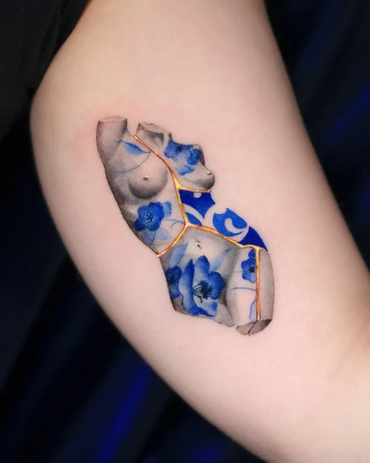 Tattoo of a blue ceramic porcelain greek statue with floral on bicep