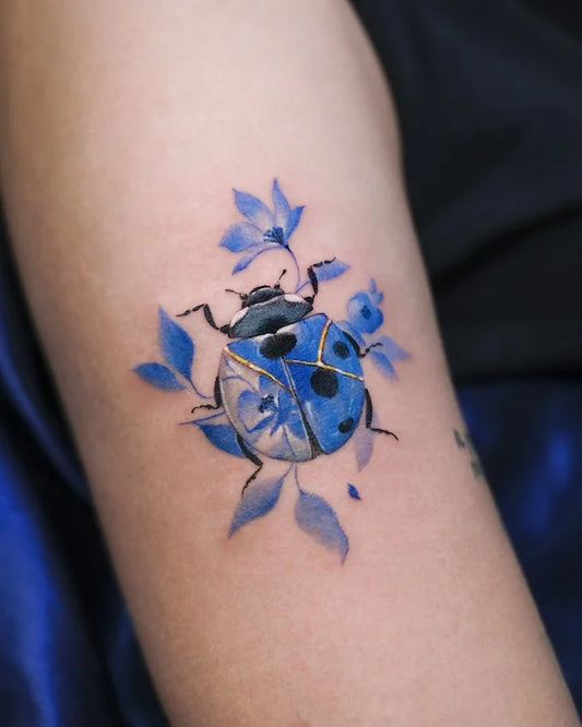 blue gold ceramic porcelain ladybug with flower color realism tattoo on woman upper arm