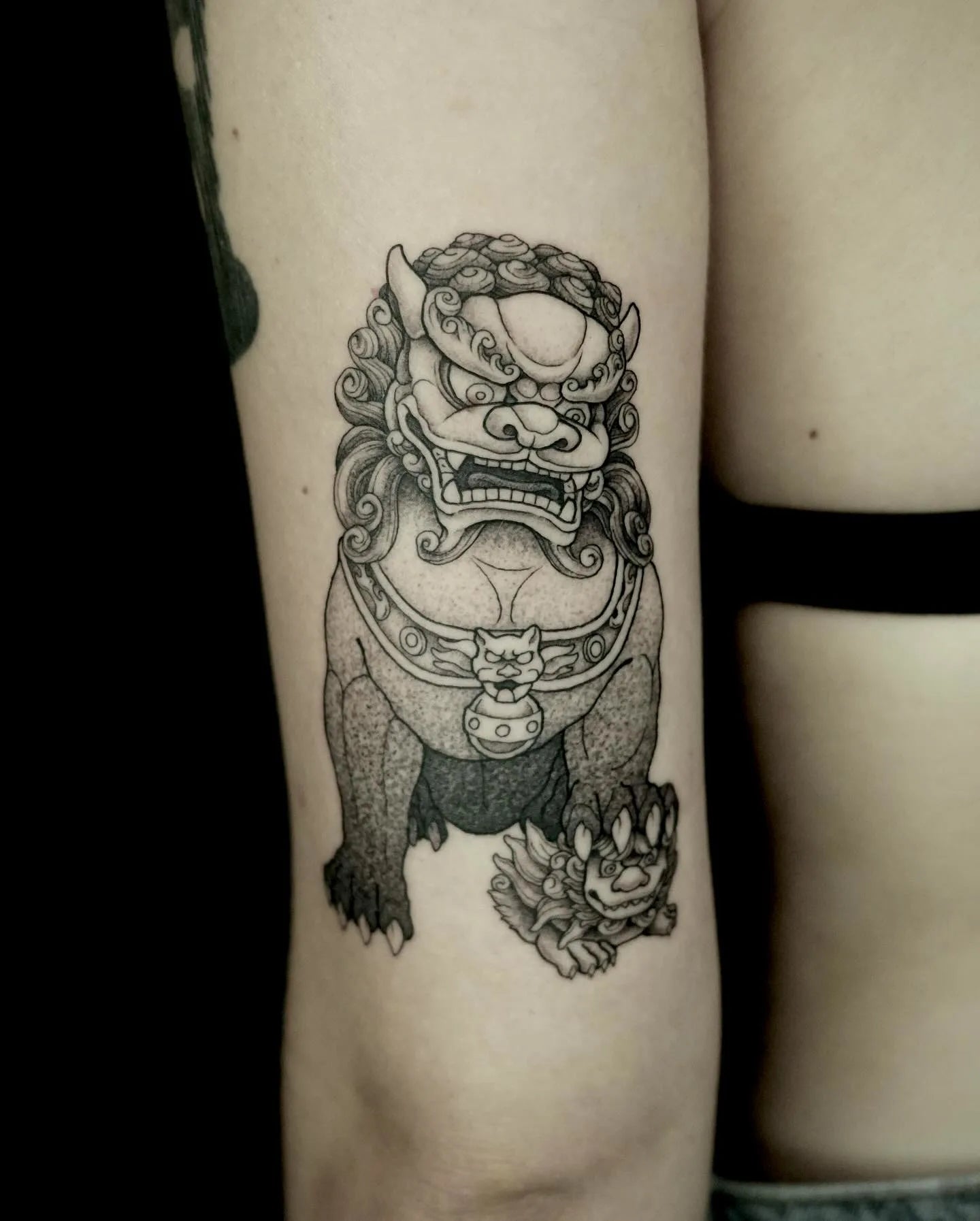 Black and grey dotwork tattoo of a traditional guardian lion foo dog on woman upper arm