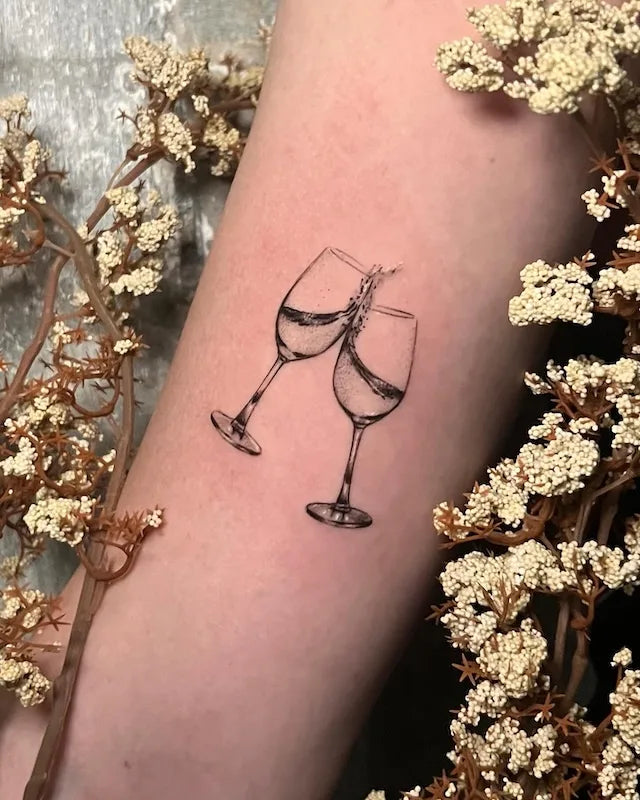 two wine glasses champange cheers minimalist tattoo on woman arm