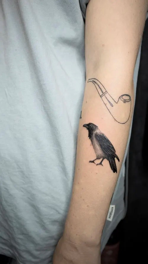 realistic crow and pipe outline arm tattoo